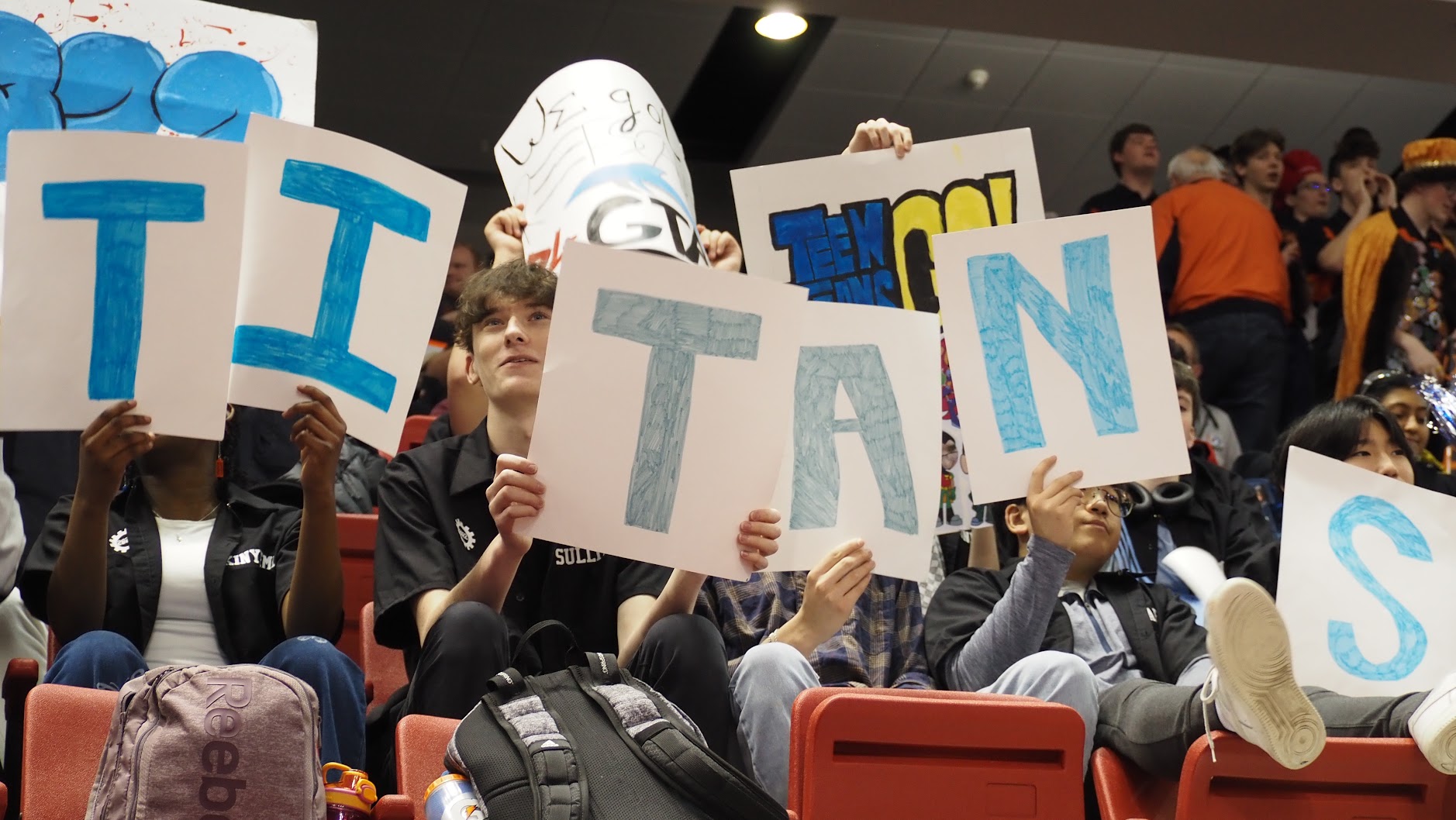 Students in the stands cheering on the Titans, holding one poster per letter.