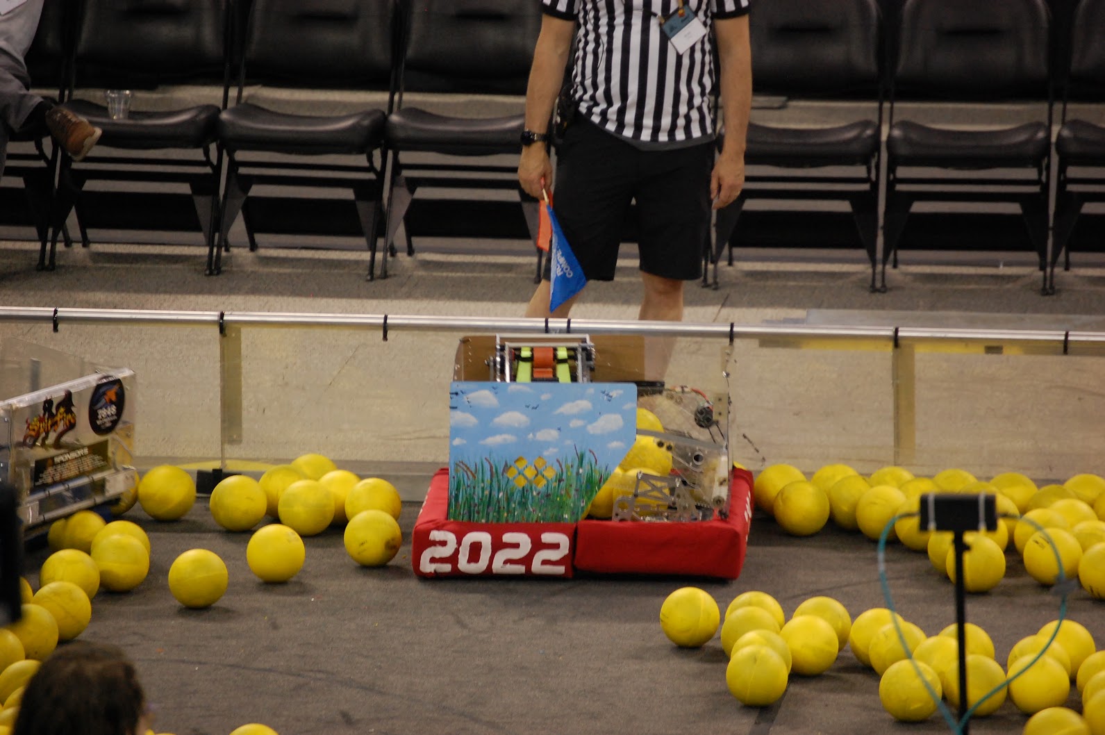 Side view of the current robot on the field with game pieces in and around it.